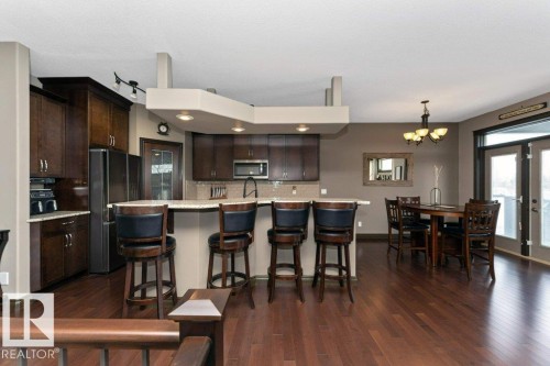 Open-concept living area with dark wood flooring, a kitchen island with seating, dark wood cabinetry, and a dining area with direct outdoor access via French doors - 33 Hillcrest Point(E), Fort Saskatchewan, AB - Indoor