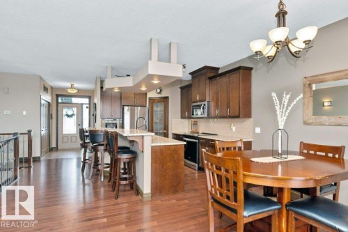 The property offers an open-concept layout with hardwood floors throughout, a kitchen featuring dark wood cabinetry and stainless steel appliances, and a dining area with a chandelier - 33 Hillcrest Point(E), Fort Saskatchewan, AB - Indoor Photo Showing Dining Room
