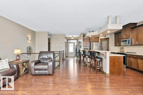 The property features hardwood floors throughout, a kitchen with dark wood cabinetry, stainless steel appliances, and a tiled backsplash - 33 Hillcrest Point(E), Fort Saskatchewan, AB - Indoor Photo Showing Kitchen With Stainless Steel Kitchen With Upgraded Kitchen