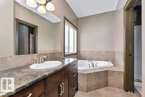 Bathroom featuring a vanity with a dark countertop and a white oval sink, a large mirror, a window, and a corner-installed tub with tiled surround - 33 Hillcrest Point(E), Fort Saskatchewan, AB - Indoor Photo Showing Bathroom