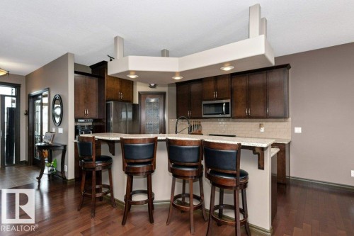 The property features a kitchen with dark wood cabinetry, stainless steel appliances, and a tiled backsplash - 33 Hillcrest Point(E), Fort Saskatchewan, AB - Indoor Photo Showing Kitchen