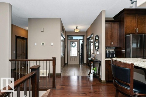 The property features rich hardwood flooring, a staircase with a dark wood banister and metal spindles, and a kitchen with dark cabinetry, stainless steel appliances, and a light-colored countertop - 33 Hillcrest Point(E), Fort Saskatchewan, AB - Indoor