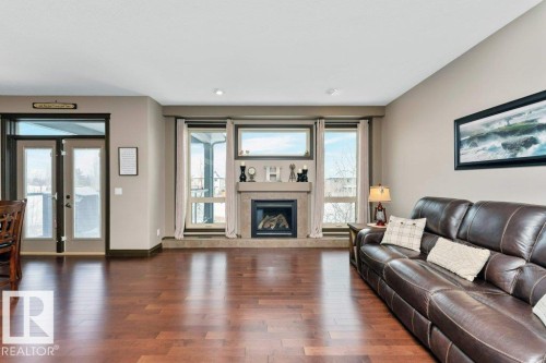 This living area features rich hardwood flooring, a stone fireplace, and ample natural light from the large windows - 33 Hillcrest Point(E), Fort Saskatchewan, AB - Indoor Photo Showing Living Room With Fireplace