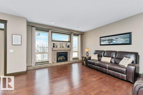 The living area features polished hardwood floors, a gas fireplace with a stone surround, and large windows providing natural light - 33 Hillcrest Point(E), Fort Saskatchewan, AB - Indoor Photo Showing Living Room With Fireplace