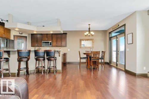 Open concept living area featuring hardwood flooring, a dining area with a chandelier, and a kitchen with an island breakfast bar, wood cabinetry, and stainless steel appliances - 33 Hillcrest Point(E), Fort Saskatchewan, AB - Indoor