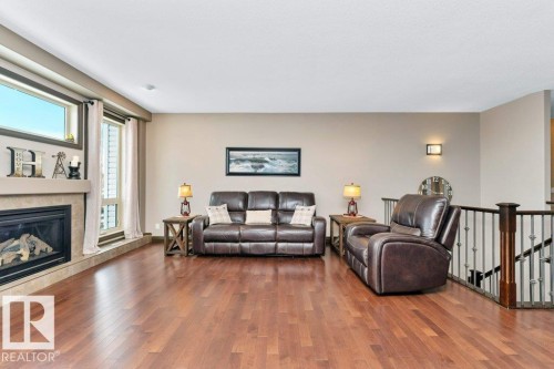 Living room featuring hardwood flooring, a fireplace with a stone surround, and large windows providing natural light - 33 Hillcrest Point(E), Fort Saskatchewan, AB - Indoor Photo Showing Living Room With Fireplace