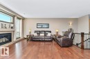 Living room featuring hardwood flooring, a fireplace with a stone surround, and large windows providing natural light - 33 Hillcrest Point(E), Fort Saskatchewan, AB  - Indoor Photo Showing Living Room With Fireplace 
