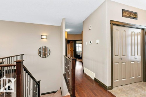 The hallway features rich hardwood flooring, a staircase with dark wood railings and metal balusters, and a closet with bifold doors - 33 Hillcrest Point(E), Fort Saskatchewan, AB - Indoor Photo Showing Other Room