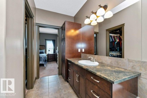 The bathroom features a vanity with a white oval sink, a wall-mounted light fixture with multiple bulbs, and a spacious mirror - 33 Hillcrest Point(E), Fort Saskatchewan, AB - Indoor Photo Showing Bathroom