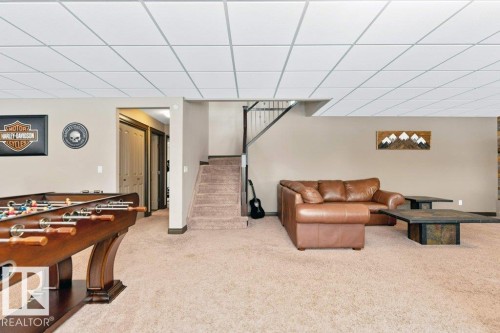 The property features a spacious room with carpeted flooring, a drop ceiling, and a staircase with carpeted treads - 33 Hillcrest Point(E), Fort Saskatchewan, AB - Indoor Photo Showing Other Room