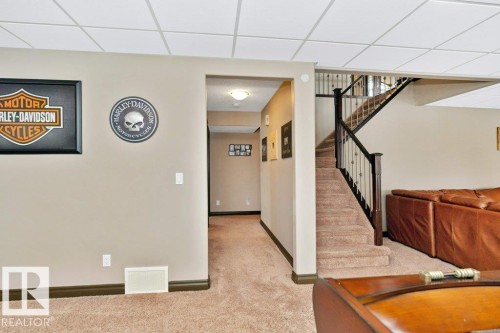 The property features a staircase with dark wood newel posts and metal balusters, and a carpeted floor - 33 Hillcrest Point(E), Fort Saskatchewan, AB - Indoor Photo Showing Other Room