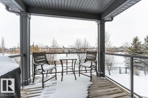 Covered balcony with a glass railing, featuring a wood deck and views of the surrounding neighborhood - 33 Hillcrest Point(E), Fort Saskatchewan, AB - Outdoor