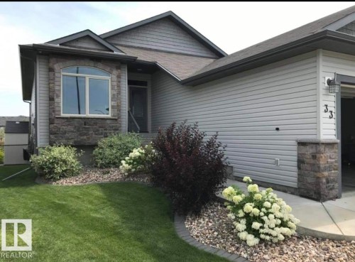 The property features a well-maintained lawn, a stone-clad facade, and tasteful landscaping with various shrubs and flowering plants - 33 Hillcrest Point(E), Fort Saskatchewan, AB - Outdoor