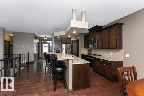 Well-appointed kitchen featuring dark wood cabinetry, a granite countertop island with seating, stainless steel appliances, and rich wood flooring - 33 Hillcrest Point(E), Fort Saskatchewan, AB - Indoor Photo Showing Kitchen With Upgraded Kitchen