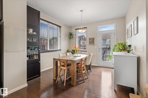 The dining area features rich hardwood floors, a large window with blinds, and a door leading to an outdoor space - 165 603 Watt Boulevard, Edmonton, AB - Indoor Photo Showing Dining Room