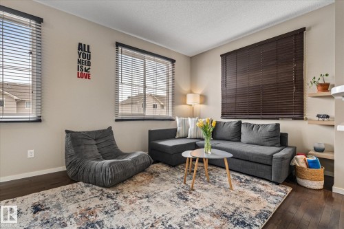 Living space featuring dark hardwood flooring, a patterned area rug, and windows with horizontal blinds - 165 603 Watt Boulevard, Edmonton, AB - Indoor Photo Showing Living Room