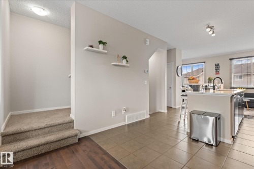 The property features a entryway with carpeted stairs and a wood floor landing, opening to a living area with tile flooring and an island with a sink - 165 603 Watt Boulevard, Edmonton, AB - Indoor