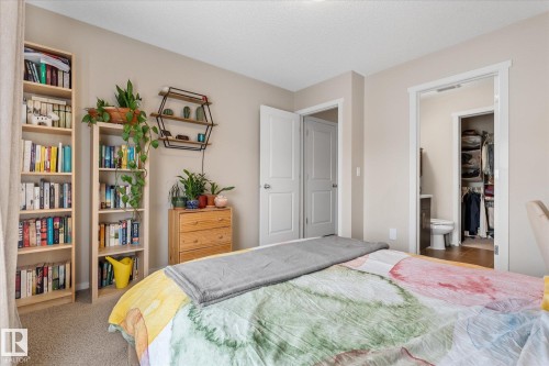 This bedroom features neutral-toned walls, carpet flooring, a natural wood dresser, and two tall bookshelves - 165 603 Watt Boulevard, Edmonton, AB - Indoor Photo Showing Bedroom