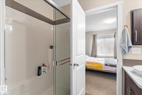 The bathroom features a shower and tub combination with a sliding glass door, a dark wood vanity with a white countertop and vessel sink, and a dark wood wall-mounted cabinet - 165 603 Watt Boulevard, Edmonton, AB - Indoor Photo Showing Bathroom