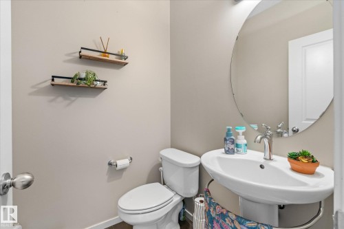 Bathroom featuring a pedestal sink with a chrome faucet, a round mirror, and a toilet - 165 603 Watt Boulevard, Edmonton, AB - Indoor Photo Showing Bathroom