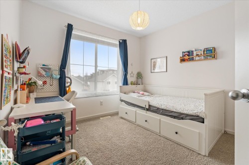 This room features a large window with blue curtains, light-colored carpet, and a white bed frame with integrated storage drawers - 165 603 Watt Boulevard, Edmonton, AB - Indoor Photo Showing Bedroom