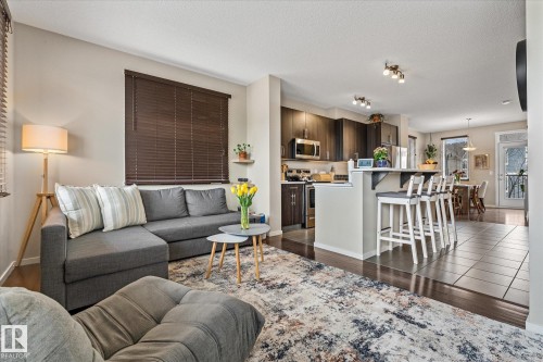 This open concept living area features hardwood floors, a kitchen with stainless steel appliances and dark cabinetry, and an island with seating - 165 603 Watt Boulevard, Edmonton, AB - Indoor Photo Showing Living Room
