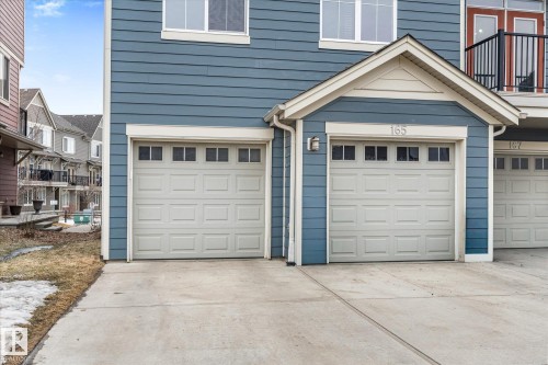 The property features a blue exterior with white trim, two white garage doors with window inserts, and a concrete driveway - 165 603 Watt Boulevard, Edmonton, AB - Outdoor With Exterior