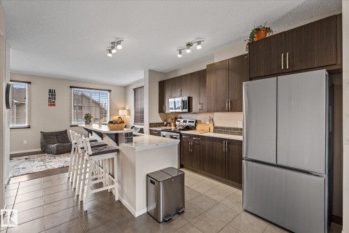 The kitchen features dark wood cabinetry, a stainless steel refrigerator, and track lighting - 165 603 Watt Boulevard, Edmonton, AB - Indoor Photo Showing Kitchen