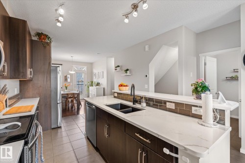 The kitchen features dark wood cabinetry, stainless steel appliances, a double basin sink with a matte black faucet, and light-colored countertops - 165 603 Watt Boulevard, Edmonton, AB - Indoor Photo Showing Kitchen With Double Sink