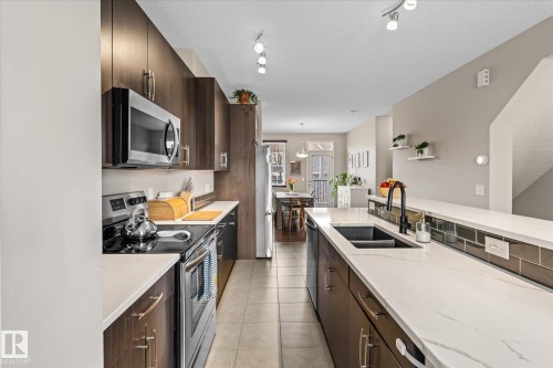 The kitchen features dark wood cabinetry, white countertops, and stainless steel appliances including a microwave and range - 165 603 Watt Boulevard, Edmonton, AB - Indoor Photo Showing Kitchen With Double Sink