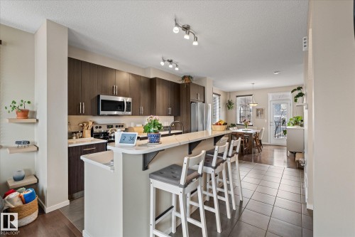 This kitchen features dark wood cabinetry, stainless steel appliances, and a light-colored island with seating - 165 603 Watt Boulevard, Edmonton, AB - Indoor Photo Showing Kitchen