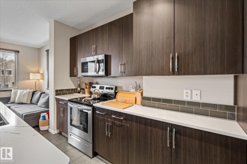 The kitchen features dark wood cabinetry, white countertops, and a subway tile backsplash - 165 603 Watt Boulevard, Edmonton, AB - Indoor Photo Showing Kitchen