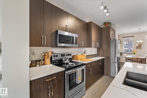 The kitchen features extensive dark wood cabinetry, white countertops, stainless steel appliances, and a tile backsplash - 165 603 Watt Boulevard, Edmonton, AB - Indoor Photo Showing Kitchen With Upgraded Kitchen