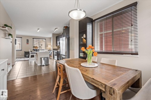 This inviting open-concept space features hardwood flooring in the dining area, which includes a window with blinds, and transitions to tiled flooring in the kitchen and living areas - 165 603 Watt Boulevard, Edmonton, AB - Indoor Photo Showing Dining Room