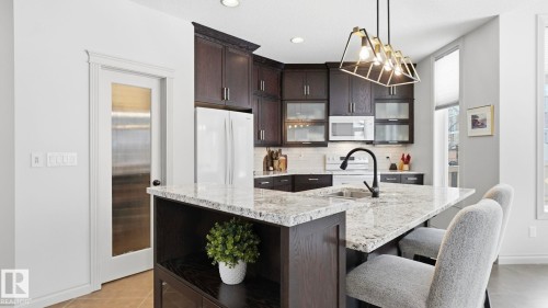The kitchen features dark wood cabinetry, white countertops, and a white subway tile backsplash, complemented by a contemporary light fixture - 131 North Ridge Drive, St. Albert, AB - Indoor