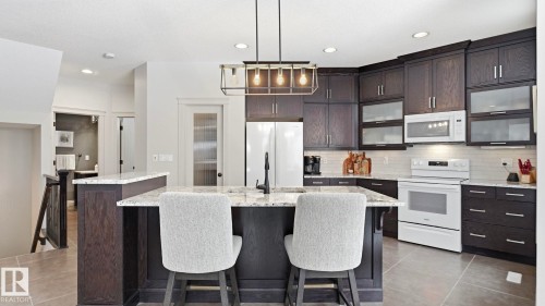 The kitchen features dark wood cabinetry, white appliances, and a central island with a granite countertop and seating - 131 North Ridge Drive, St. Albert, AB - Indoor