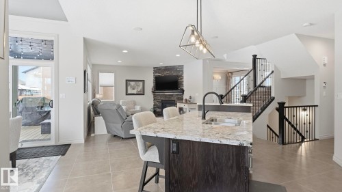 Open concept interior featuring tiled flooring, a kitchen island with a sink and pendant lighting, and a living area with a stone-clad fireplace - 131 North Ridge Drive, St. Albert, AB - Indoor Photo Showing Kitchen With Double Sink With Upgraded Kitchen