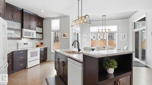 Well-appointed kitchen featuring dark wood cabinetry, white appliances, light countertops, and a central island with a sink - 131 North Ridge Drive, St. Albert, AB - Indoor Photo Showing Kitchen With Double Sink With Upgraded Kitchen