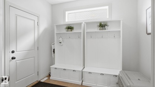 Mudroom area featuring a white paneled door with dark hardware, light wood flooring, and two white built-in storage units with shelving, hooks, and bench seating - 131 North Ridge Drive, St. Albert, AB - Indoor Photo Showing Other Room