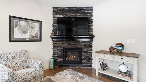 Living area featuring a natural stone fireplace with a black mantel, an inset fireplace, and hard surface flooring - 131 North Ridge Drive, St. Albert, AB - Indoor Photo Showing Living Room With Fireplace