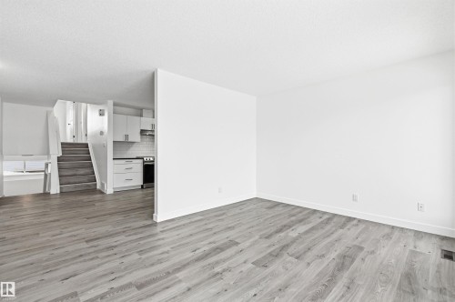 The property features a bright living area with light-toned flooring, leading to a kitchen with white cabinetry and appliances, and a staircase with carpeted treads - 16223 55A Street, Edmonton, AB - Indoor Photo Showing Other Room