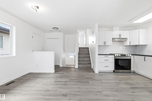 The property features an open-concept living area with light-toned flooring, a kitchen with white cabinetry and black countertops, and a modern stainless steel range - 16223 55A Street, Edmonton, AB - Indoor Photo Showing Kitchen With Upgraded Kitchen