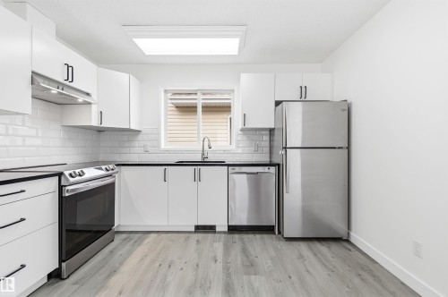 The kitchen features white cabinetry, black countertops, and stainless steel appliances including a range, dishwasher, and refrigerator - 16223 55A Street, Edmonton, AB - Indoor Photo Showing Kitchen