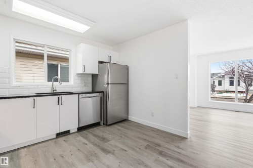 The kitchen features white cabinetry with black hardware, a stainless steel refrigerator, and a stainless steel dishwasher - 16223 55A Street, Edmonton, AB - Indoor Photo Showing Kitchen