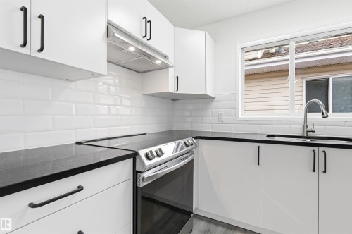 The kitchen features white cabinetry with black hardware, dark countertops, a white subway tile backsplash, and a stainless steel range - 16223 55A Street, Edmonton, AB - Indoor Photo Showing Kitchen With Double Sink