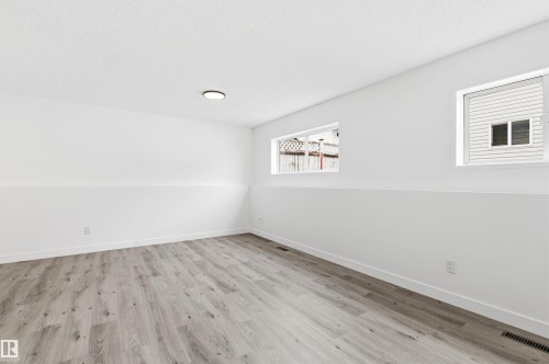 This room features light-toned wood-style flooring and two windows, providing natural light - 16223 55A Street, Edmonton, AB - Indoor Photo Showing Other Room