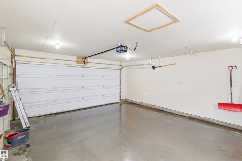 The property features an attached garage with a concrete floor, a white overhead door, and exposed ceiling joists - 16223 55A Street, Edmonton, AB - Indoor Photo Showing Garage