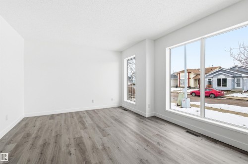 The property features large windows providing views of the surrounding neighborhood, light-colored walls, and gray wood-style flooring - 16223 55A Street, Edmonton, AB - Indoor Photo Showing Other Room