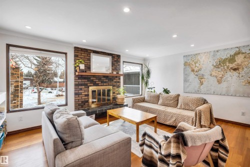Living area featuring hardwood floors, a brick fireplace with a mantel, and large windows providing natural light - 4208 89 Street Nw, Edmonton, AB - Indoor Photo Showing Living Room With Fireplace