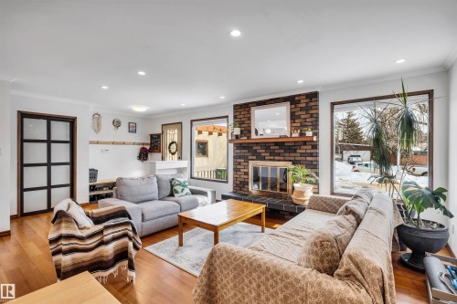 Living area featuring hardwood floors, a brick fireplace, and large windows providing natural light - 4208 89 Street Nw, Edmonton, AB - Indoor Photo Showing Living Room With Fireplace